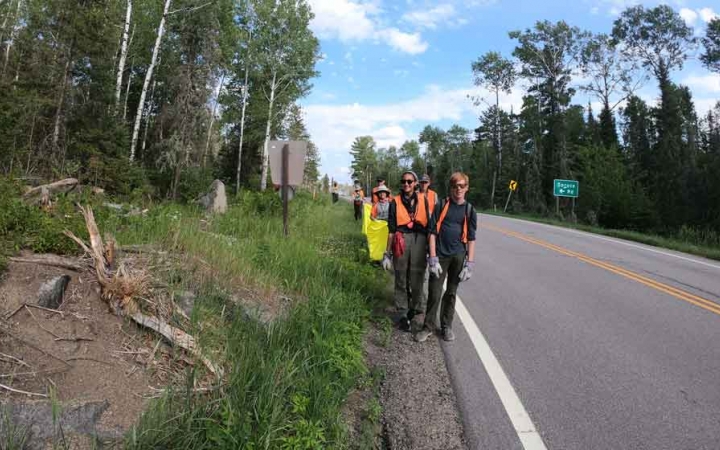 a group of students wearing brightly colored vests participate in a service project beside a road
